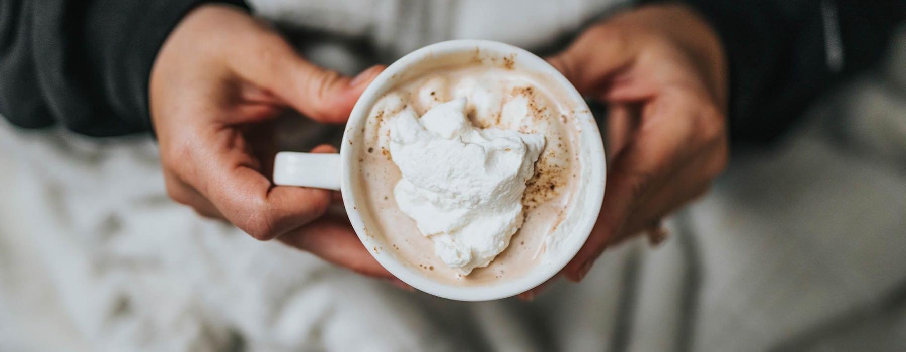 a person, in bed, holding a cup of coffee